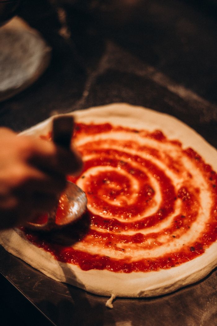 Close-up of tomato sauce being spread on pizza dough, showcasing food preparation artistry.
