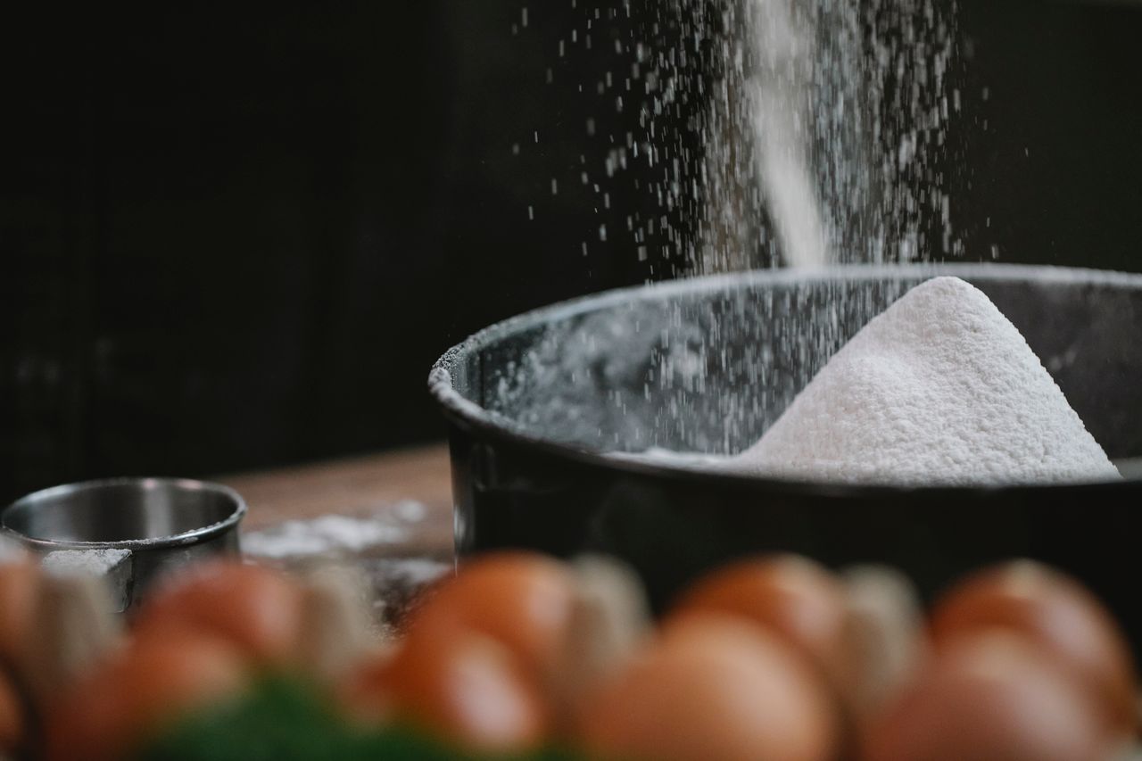 Process of preparing dough with flour pouring into baking dish placed near box of eggs